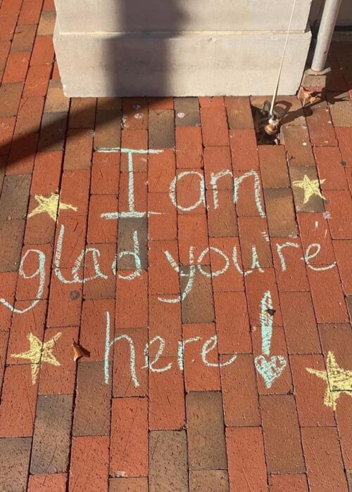 Brick with words in blue chalk: "I am glad you're here!" and yellow stars