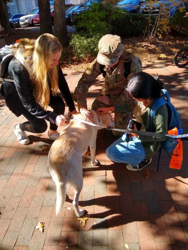 Three students, including one ROTC in uniform, happily clustered around and petting Willow