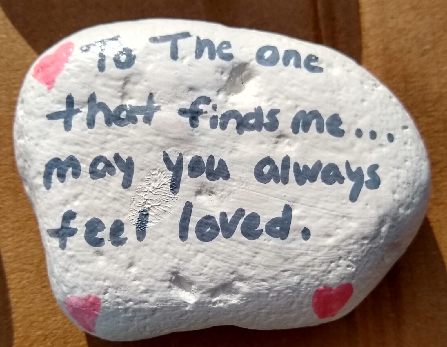 Rock painted white that says, "To the one who finds me, may you always feel loved." with pink and red hearts