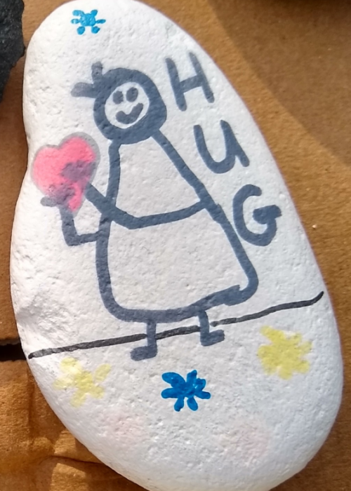 A white painted rock with a smiling figure holding a heart and the word "HUG"