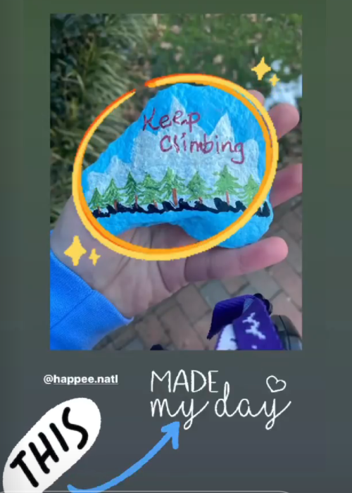 A hand holding a painted rock that says "Keep climbing!" on top of mountains on an Instagram story that tagged HAPPEE.natl, followed by the words "made my day." This story has been reposted as a story by HAPPEE.natl with the added words "IT MADE OURS TOO!!!"