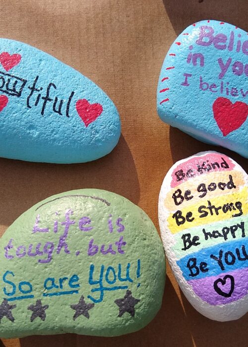 Four painted rocks that say "BeYOUtiful", "Believe in yourself - I believe in you," "Life is tough, but so are YOU," "Be kind, Be good, Be strong, Be happy, Be YOU!"