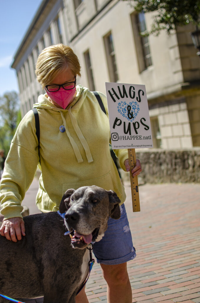 A volunteer holding a Hugs & Pups sign and petting blue