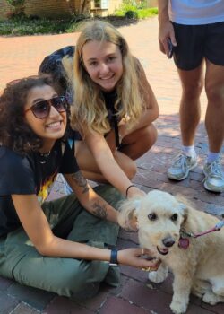 Two students sitting in front of and petting Ewie, and small golden doodle