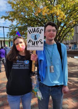 Cathy holding a "Hugs & Pups" sign standing with a student