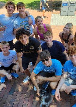 Tiny Lucky surrounded by 11 students, mostly (or all?) members of the Carolina swim team