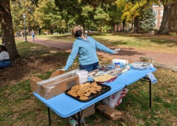 A volunteer posing behind a table full of Birthday baked goods